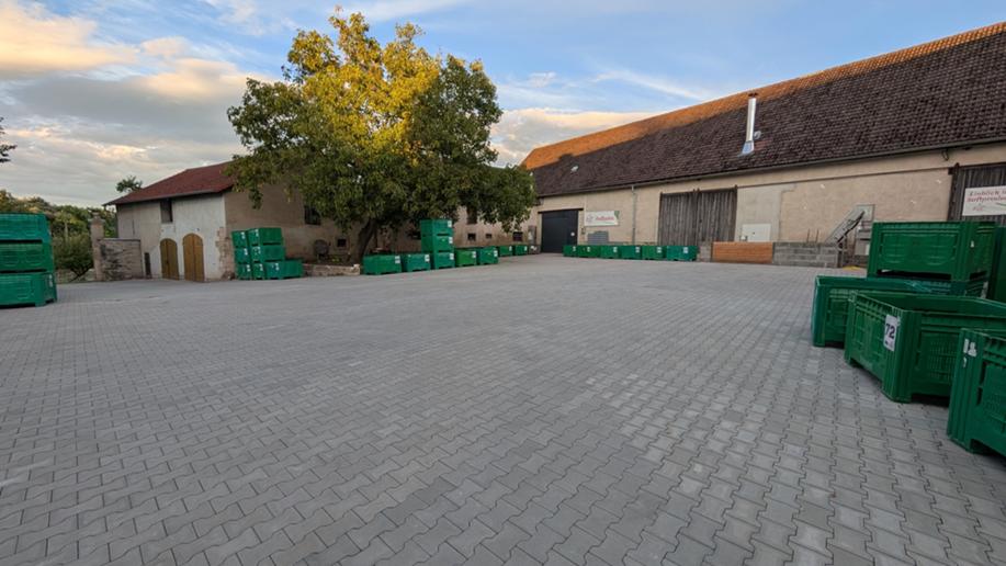 Neu gepflasterter Hof der Kelterei mit grünen Obstkisten am Rand